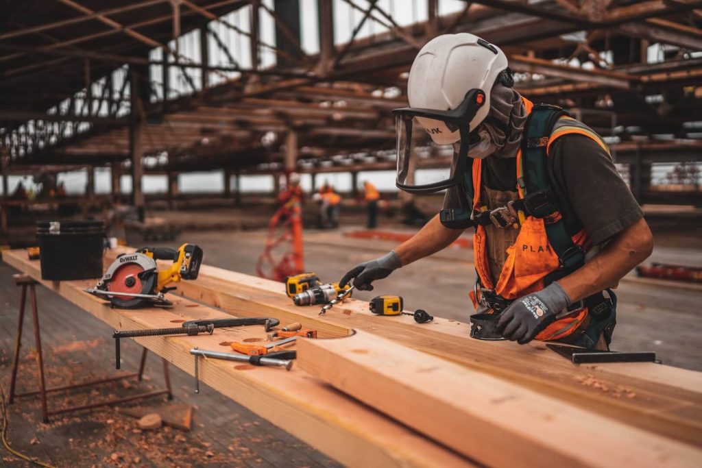 man in orange and black vest wearing white helmet holding yellow and black power tool